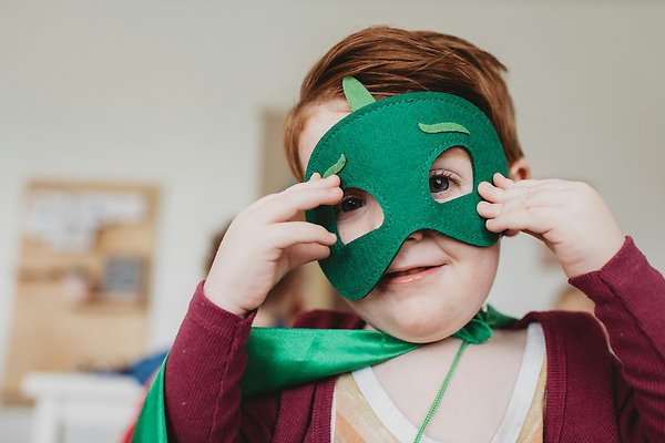 Ett litet barn som klätt ut sig med grön ansiktsmask av filt och en mantel av siden