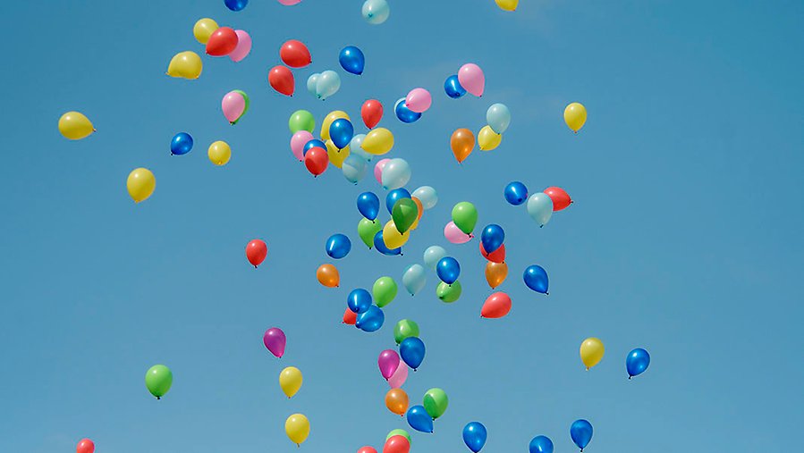 Ballonger i olika färger som stiger emot en blå himmel.